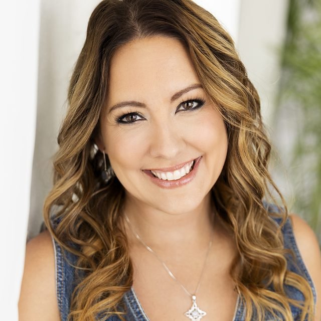 Kelly Pasztor smiling in a denim dress and star pendant